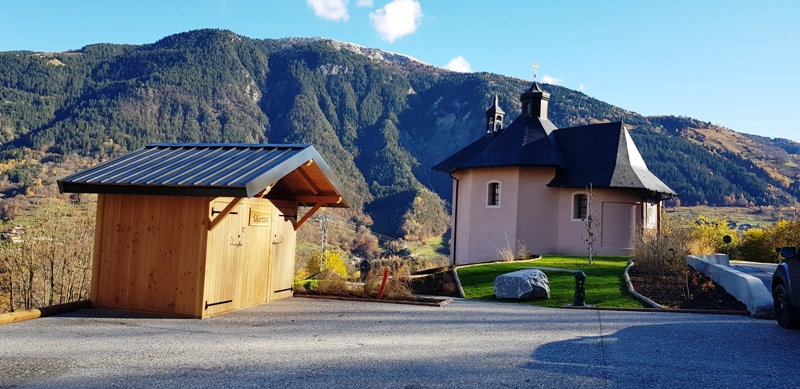 Sur le parking il y a les toilettes sèches double avec la chapelle en arrière plan